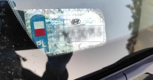 Ingerencja w naklejkę rejestracyjną pojazdu naklejka rejestracyjna pojazdu, zniszczona i częściowo odklejona od szyby auta