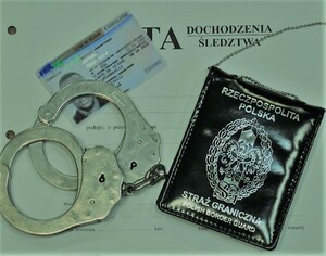 podrobiona francuska karta pobytu leży ka aktach sprawy , obok leży okładka legitymacji SG oraz metalowe kajdanki