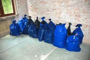 Zabezpieczona przez Straż Graniczną krajanka tytoniowa w pustym pomieszczeniu stoją duże worki koloru niebieskiego, w których znajduje się krajanka tytoniowa