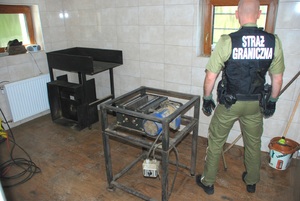 Zatrzymano sprzęt do cięcia tytoniu funckjoanriusz Straży Granicznej stoi koła zatrzymanej krajalnicy tytoniu
